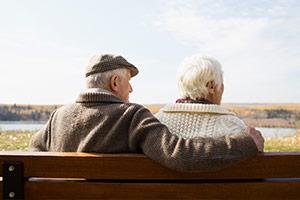 An elderly couple sitting close together looking out into the distance.