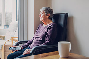 An elderly woman in a home suffering from financial abuse is staring out the window.